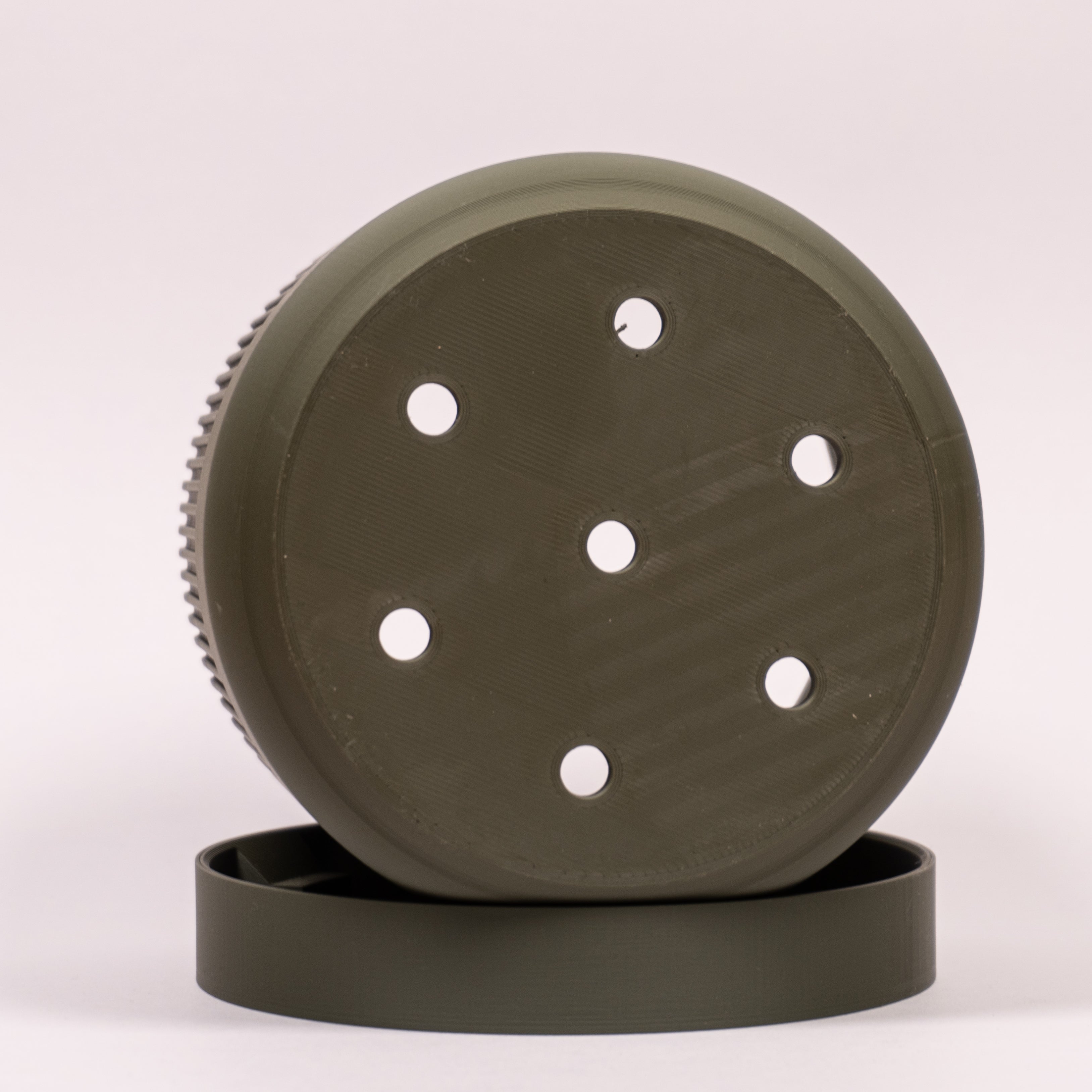 Nærbillede af grøn Seedling urtepotteskjuler Ø11cm på siden i drypbakken, med fokus på drænhullerne i bundens midte.