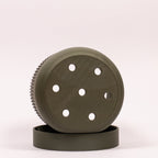 Foto af grøn Seedling urtepotteskjuler Ø9cm, placeret på siden i drypbakken, hvor de funktionelle drænhuller er synlige.