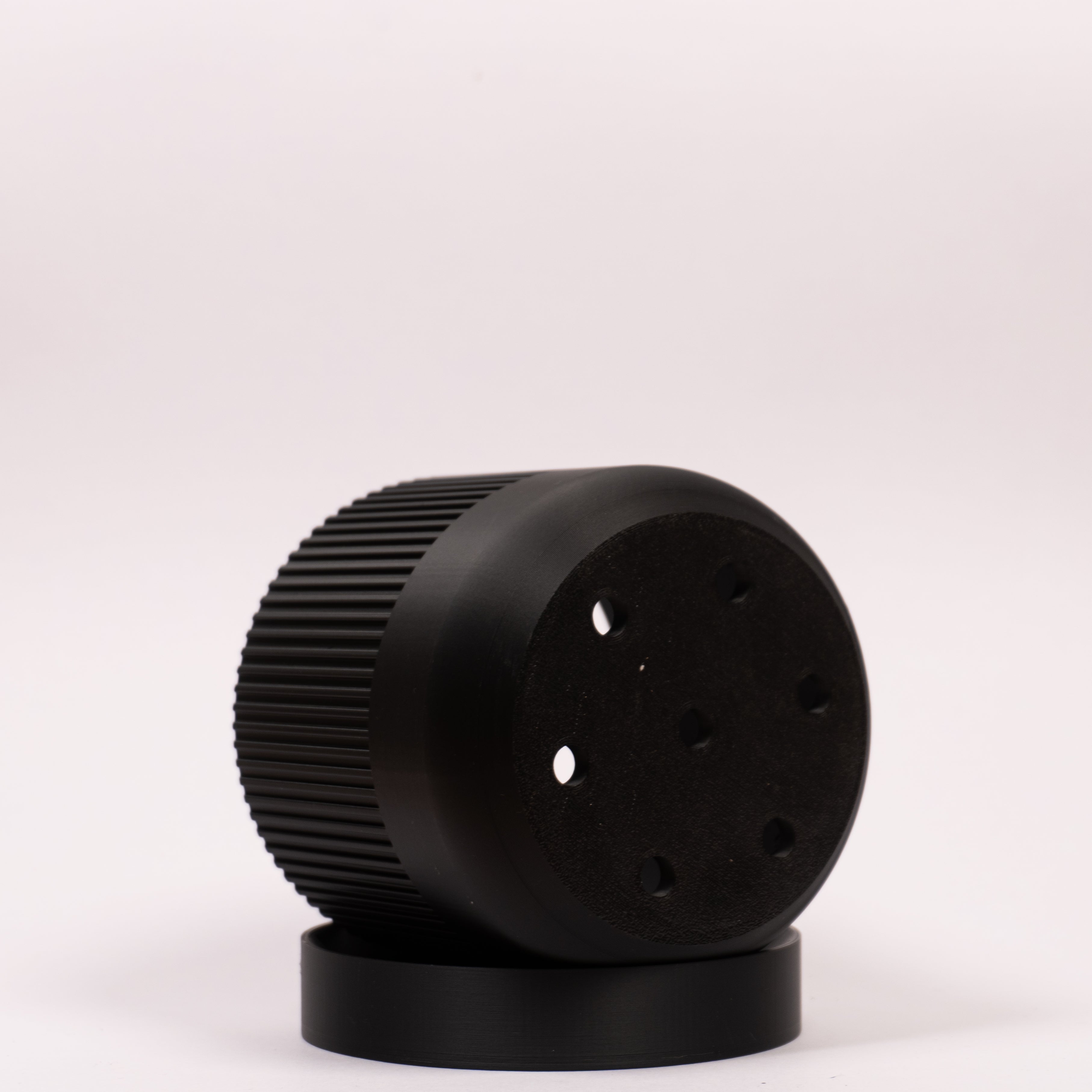 Foto af sort Seedling urtepotteskjuler Ø9cm, placeret på siden i drypbakken, hvor drænhullerne i bunden er synlige.